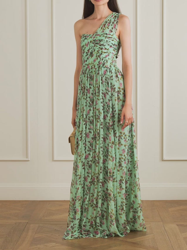 Crafted from luxuriously pleated silk-chiffon, this elegant gown features a romantic floral and leaf print. The sophisticated one-shoulder design wraps gracefully across the bust with a built-in corset for a flattering silhouette, transitioning into an effortlessly flowing skirt that cascades to the floor from the empire waist.