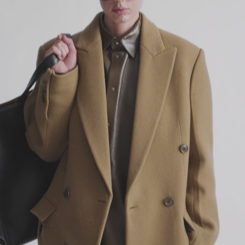 This refined man's coat by Phoebe Philo combines luxury and contemporary tailoring in a sumptuous tobacco cashmere wool blend. Featuring a double-breasted silhouette with inverted sleeves and a lightly structured shoulder, the design creates an elegant, modern profile. The dropped waist contour and front slits enhance movement and sophistication. Expertly pressed and partially lined, the double-faced construction with glossy satin finish delivers exceptional quality and a polished appearance. 