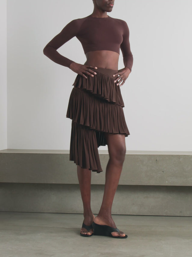 Inspired by architectural form and the iconic spiral of the Guggenheim Museum, this tiered asymmetric mini skirt channels Alaïa's Winter '25 collection. Crafted from luxuriously soft jersey, cascading layers create a dynamic silhouette that descends to an asymmetric hem—a wearable interpretation of modernist design. The interplay of structure and fluidity makes this piece both a statement and a second skin.